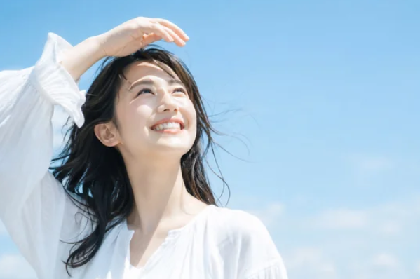 白い服で風を受けながら青空に向かって笑顔を向ける女性 ─ Mani Padme ありのまま自己受容と変容を超えた先の魂の喜びと人生変革コンサルティング